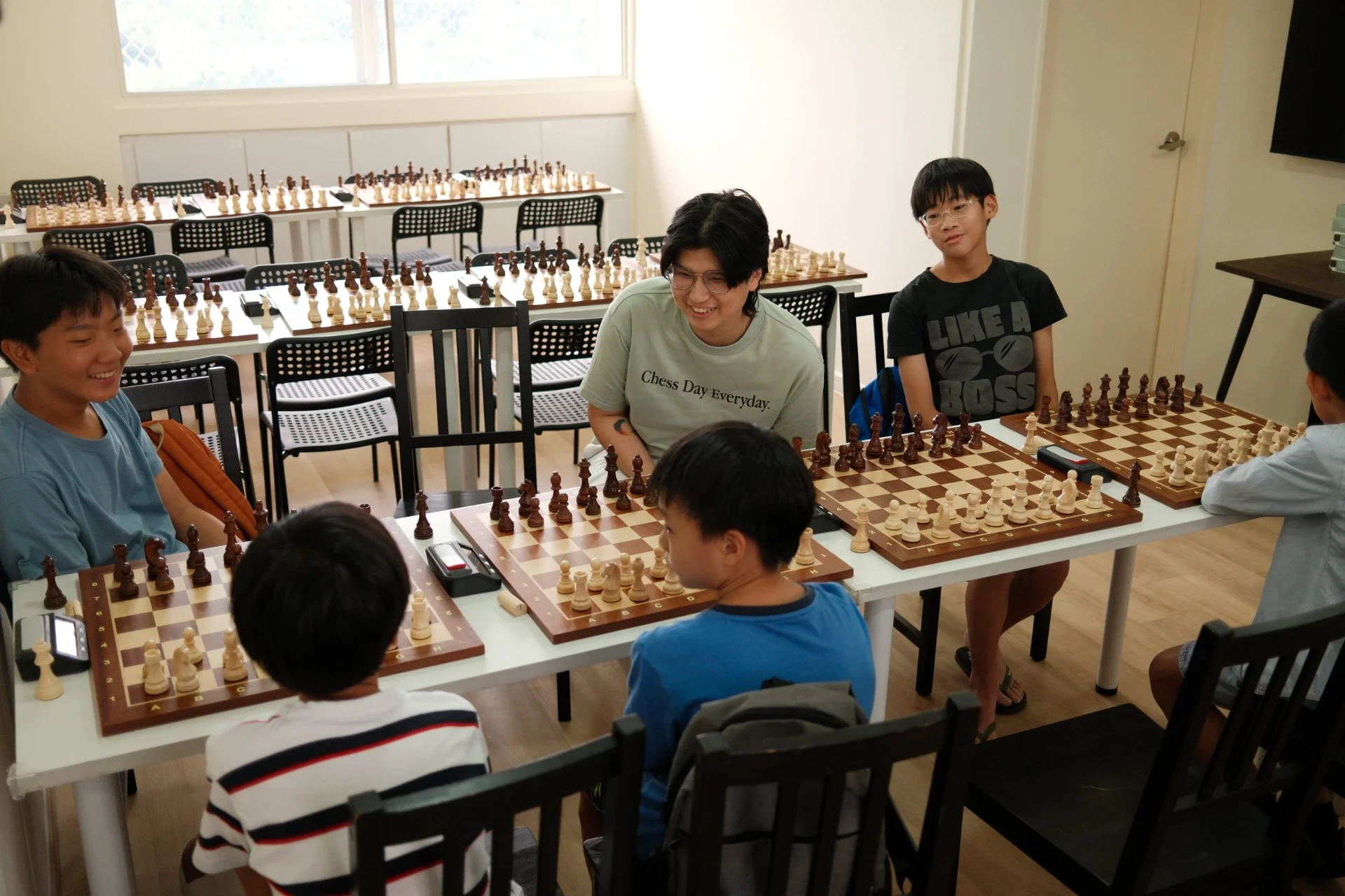Children gathered around chess boards in a bright classroom — sample chess learning environment.